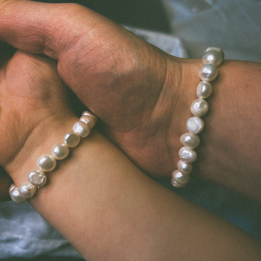 Two hands holding each other wearing pearl bracelets. One a child and one an adult. 