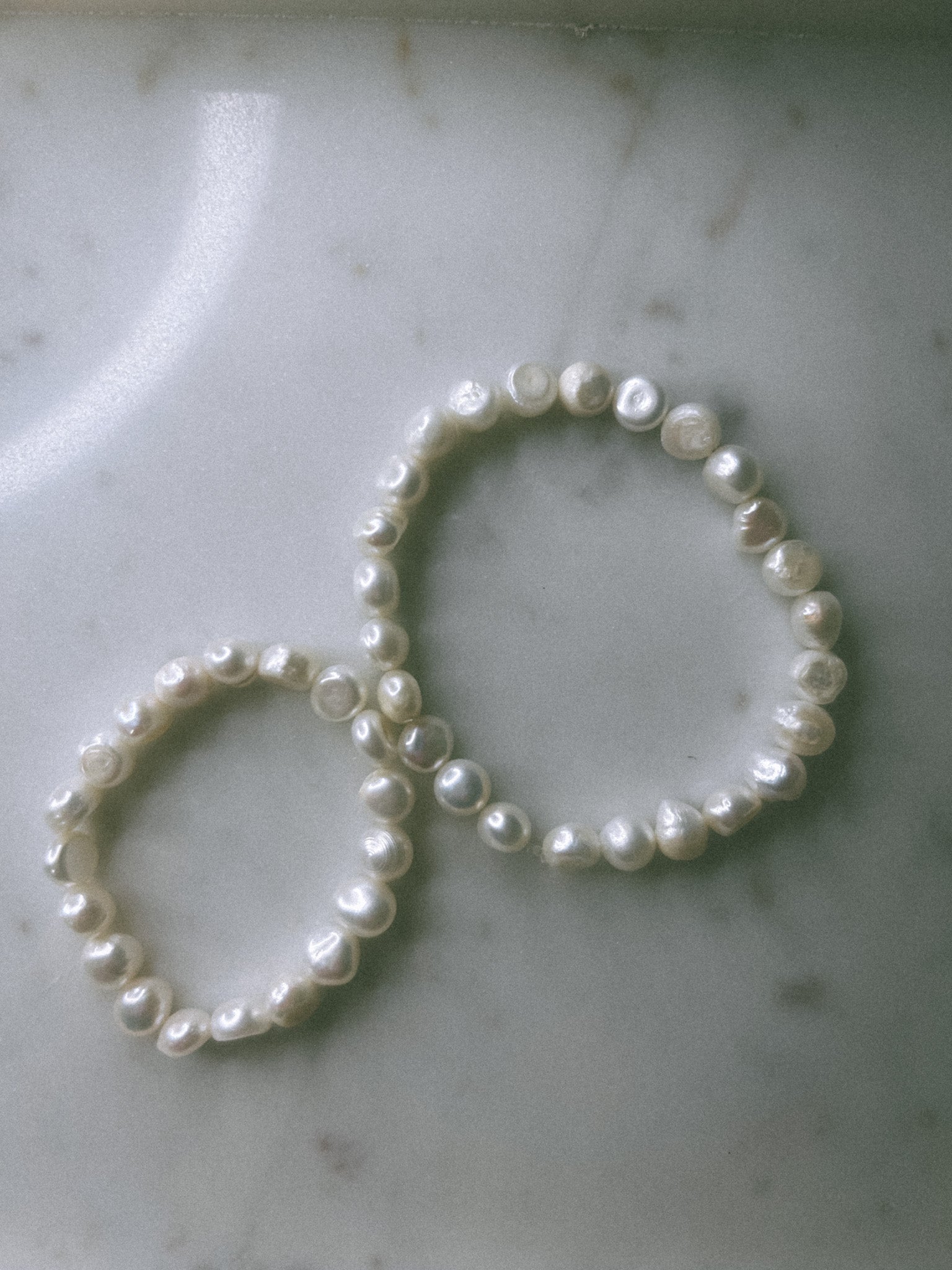 Two pearl hair ties on a marble surface